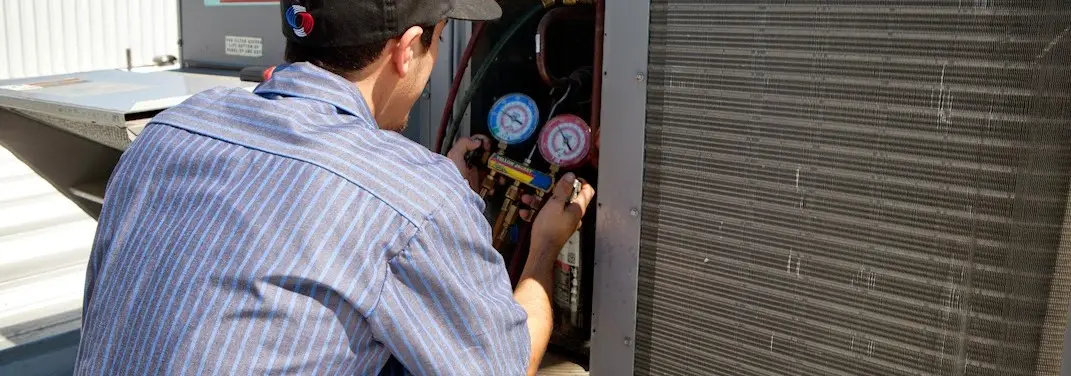 HVAC technician servicing a condenser unit in Kinross